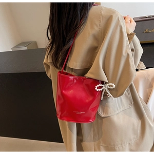 Detail of red leather bucket bag with pearl bow charm worn as a chic shoulder bag