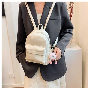 Detail of a beige PU leather backpack with a pink plush monster charm and silver zippers