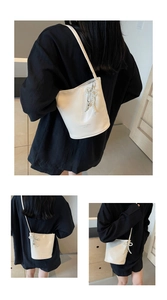 Detailed view of creamy white bucket bag with pearl bow charm and shoulder strap