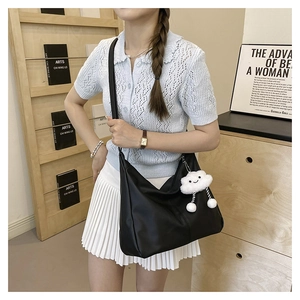 Close-up of black crescent hobo bag with white cloud plush charm in lifestyle setting