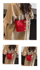 Detail of red glossy bucket bag with pearl bow charm and shoulder strap