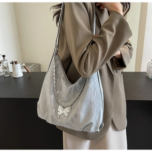 Silver pleated hobo bag with butterfly chain charm shown on model in a modern cafe setting