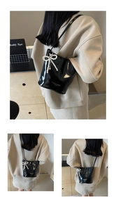 Glossy black bucket bag detail with white fashion lettering and pearl bow charm