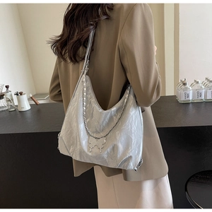 Close-up of silver pleated tote bag with chain strap and metallic butterfly charm detail