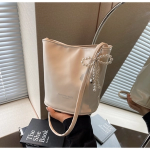 Close-up of cream bucket bag featuring fashion text print and pearl bow charm accessory