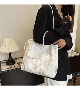 Detail of white tote bag featuring green butterfly prints and braided handles on model