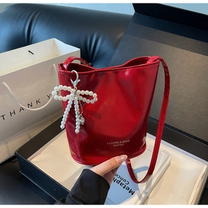 Detail of red patent leather bucket bag with pearl bow charm in a black gift box