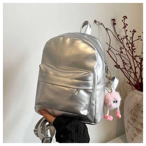 Silver metallic backpack with a cute pink plush monster keychain held by hand