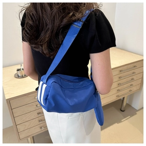 Detailansicht einer blauen Nylon-Umhängetasche mit weißen Streifen und breitem Schultergurt