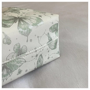 Detailed close-up showing stitching and green butterfly print on the beige tote bag