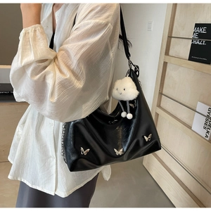 Detail view of black pleated tote bag with silver butterfly clips and a white plush charm