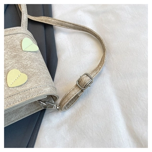 Close-up of matte textured crossbody bag with heart patches and adjustable strap details