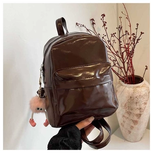 Detail view of a dark brown glossy PU mini backpack featuring a pink plush toy charm