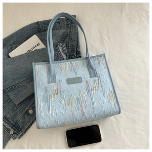 Detail of light blue leather tote bag featuring colorful wavy embroidery and logo
