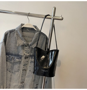 Close-up of glossy black patent leather bucket bag with white fashion text and shoulder strap