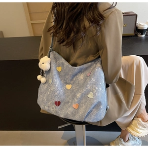 Détail d'un sac cabas en denim bleu clair avec patchs cœur colorés et breloque nuage