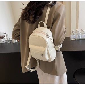 Detail eines cremefarbenen PU-Minirucksacks mit Steinstruktur, getragen zum Blazer im Erdton