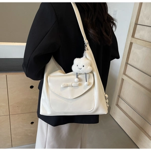 Detail of cream leather shoulder bag with bow, plush cloud charm, and adjustable strap