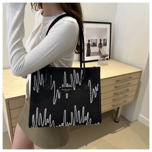 Macro view of black leather tote bag featuring colorful wavy embroidery and chic brand tag