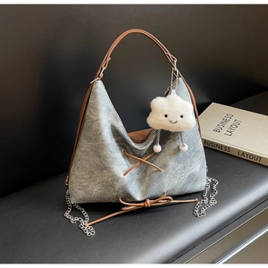 Dettaglio borsa tote in denim grigio vintage con manici in pelle, catena e ciondolo