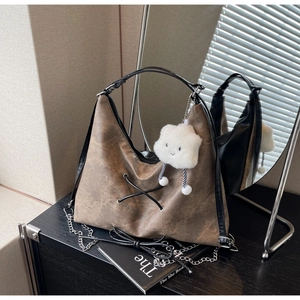 Dettaglio borsa hobo in pelle marrone vintage con corde e ciondolo in peluche bianco