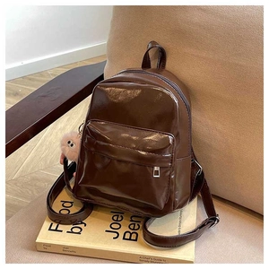 Detail view of glossy brown faux leather backpack with plush ball charm on book decor