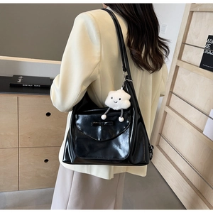 Detail of black patent leather tote bag with bow pocket and white cloud plush charm