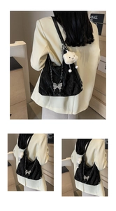 Close-up of black pleated underarm bag with silver butterfly chain and plush charm