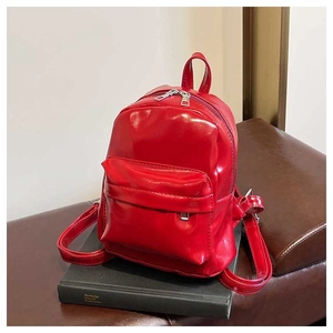 Detail of red shiny PU leather mini backpack with silver zippers on black books