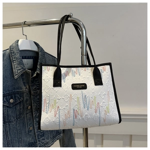Detail of white tote bag featuring colorful embroidered waves and black leather trim accents