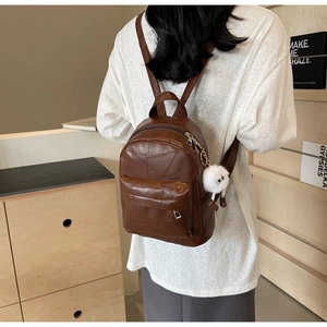 Detailaufnahme des braunen Patchwork-Rucksacks mit weißem Plüsch-Anhänger an der Seite