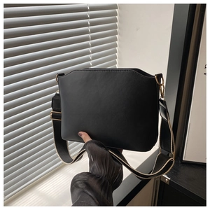 Detail of black leather shoulder bag showing wide strap and gold hardware accents