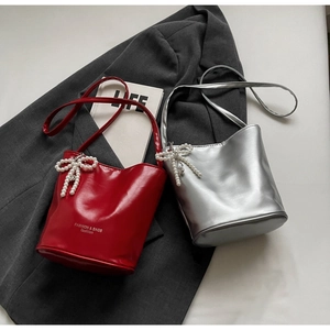 Close-up of red and silver bucket bags with pearl bow charms on a gray blazer
