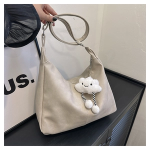 Beige faux leather hobo bag with a white fuzzy cloud charm on a black surface