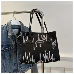 Detail of black tote bag with wavy embroidery and monogram pattern hanging on a rack