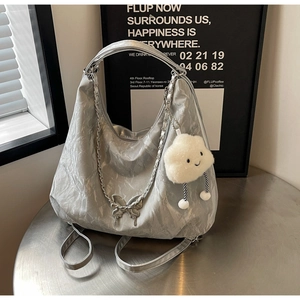 Detail of silver pleated tote bag with chain strap and butterfly charm on a metal table