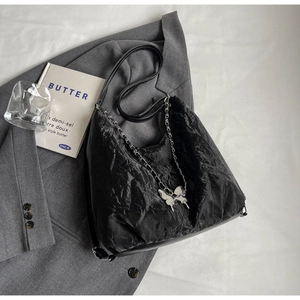 Detail of black pleated tote bag featuring silver chain strap and metallic butterfly charm