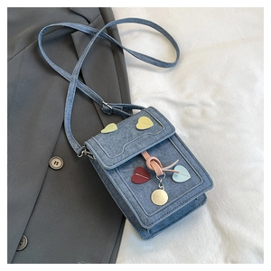 Detail of blue denim crossbody phone bag with colorful heart patches and pink lace-up décor