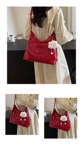 Detail of red glossy shoulder bag with bow flap and white plush cloud charm accessory