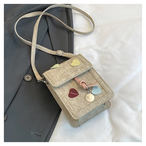 Detail of beige textured fabric crossbody bag with colorful heart patches and gold pendant