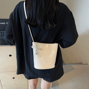 Minimalist cream white bucket bag with pearl bow charm worn by a model in a casual setting