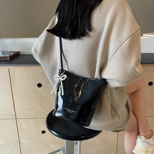 Glossy black bucket bag with pearl bow accessory and high-shine finish on model