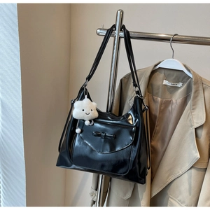 Close-up of a black glossy PU tote bag with a bow detail and a white plush cloud charm