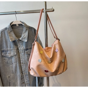 Détail du sac fourre-tout rose en cuir souple avec écussons cœurs 3D sur fond denim