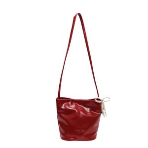 Glossy red bucket bag with pearl bow accessory and sleek leather shoulder strap