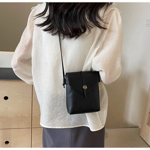 Rear view of black lychee-textured crossbody phone bag with gold clasp on model