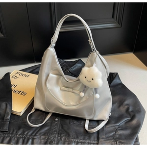 Silver-grey hobo tote bag with bow pocket and white cloud plush charm on a leather jacket