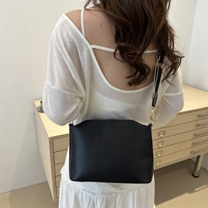 Minimalist black matte leather shoulder bag with gold buckle and wide strap, back view model shot
