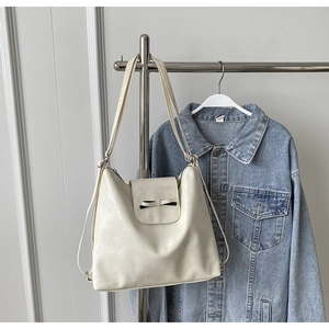 Detalle de un bolso tote crema con lazo negro colgado junto a una chaqueta de mezclilla
