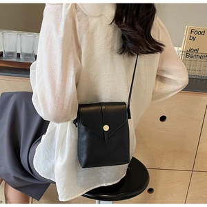 Close-up of black lychee grain leather crossbody bag with a round gold metal buckle